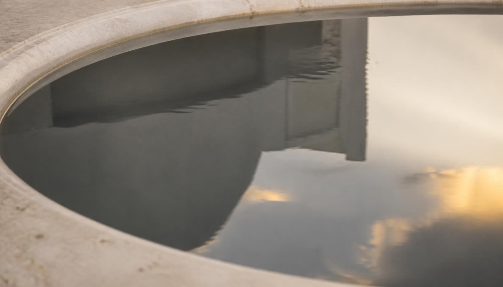 Still water in a pale stone basin reflecting soft light