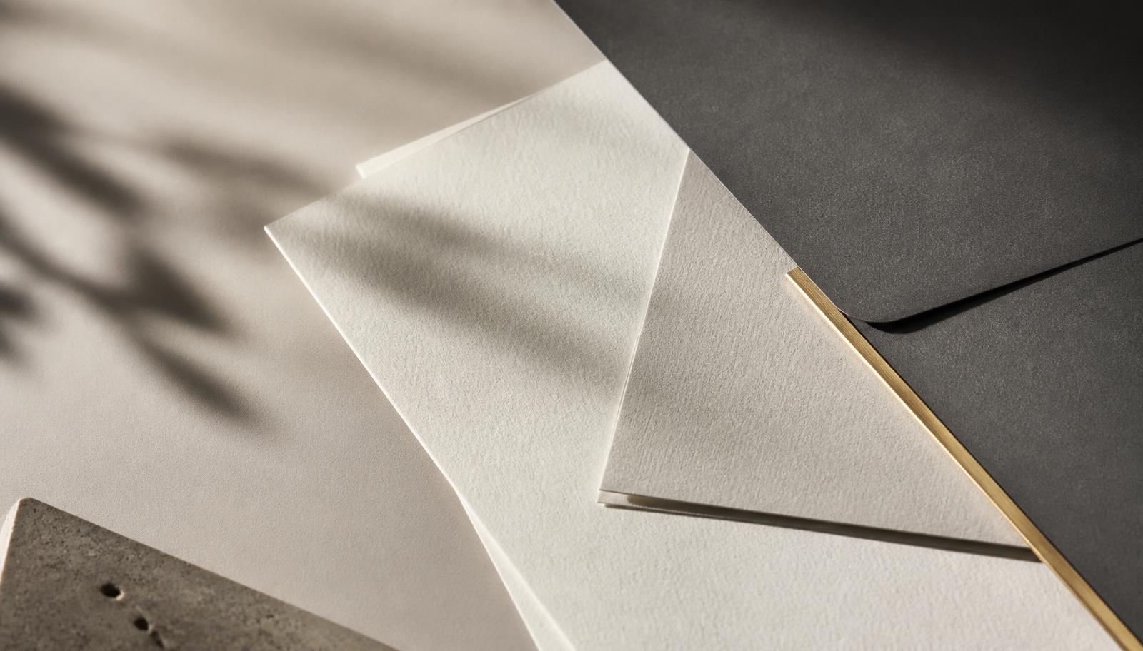 Sheets of warm white paper and a charcoal folder in raking light